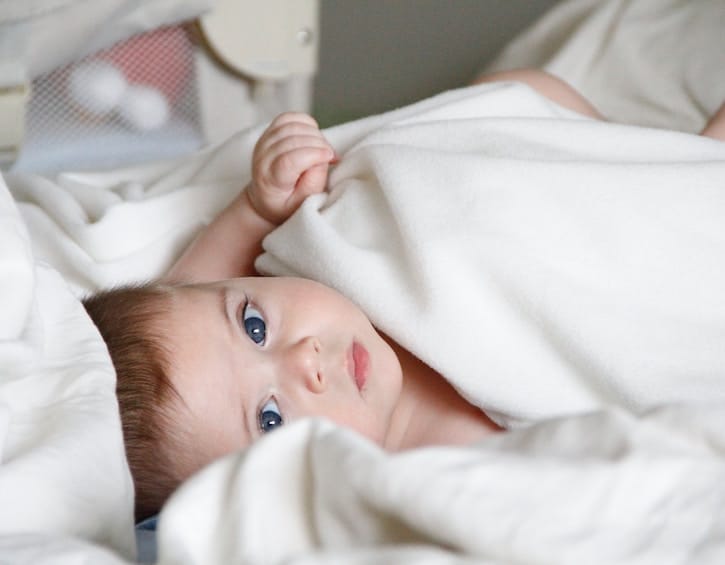 baby laying in a white bed sheet