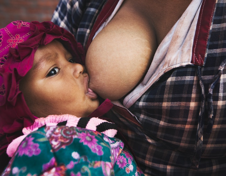 toddler with pink hat breastfeeding