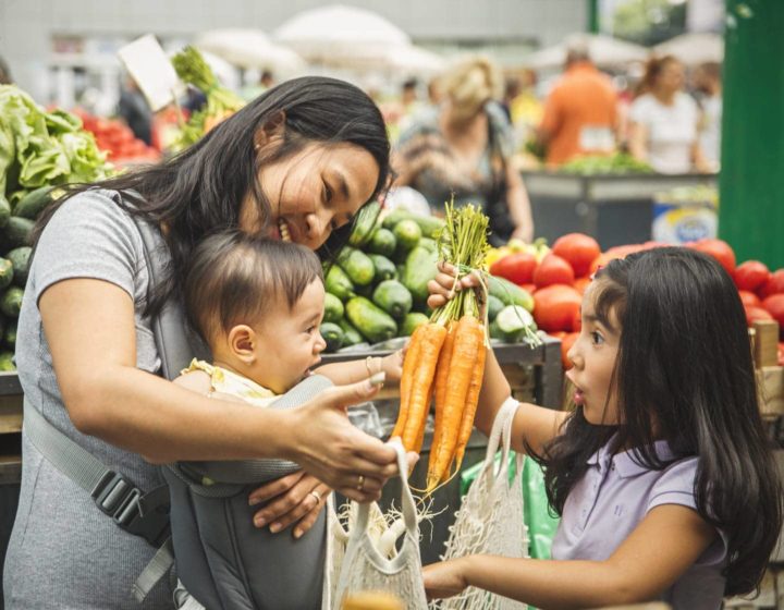 Mum shopping for organic vegetables with baby and daughter