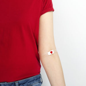a woman in a red t-shirt with a small bandaid on her inner elbow after a blood donation