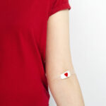 a woman in a red t-shirt with a small bandaid on her inner elbow after a blood donation