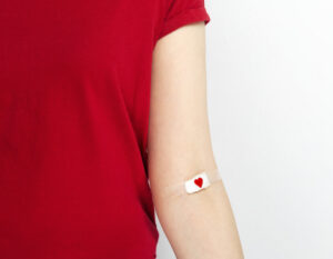 a woman in a red t-shirt with a small bandaid on her inner elbow after a blood donation