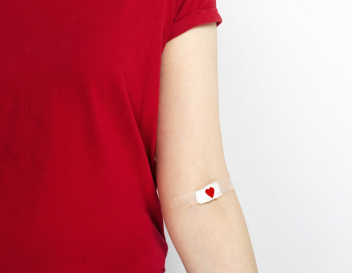 a woman in a red t-shirt with a small bandaid on her inner elbow after a blood donation