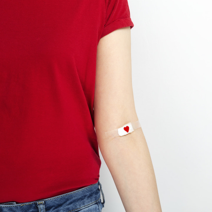 a woman in a red t-shirt with a small bandaid on her inner elbow after a blood donation