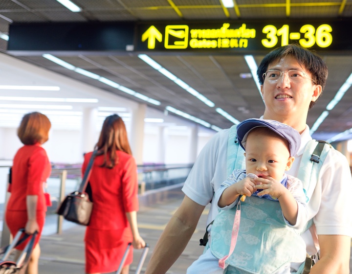 Smiling asian father holding Cute little Asian teething 1 year old baby boy child in a baby carrier, Dad and son standing near sign at airport