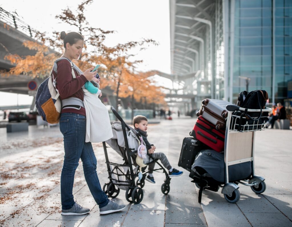single mother travels with baby in carrier, toddler in stroller and carry on luggage