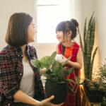 Young mother and daughter planting cactus in the room.