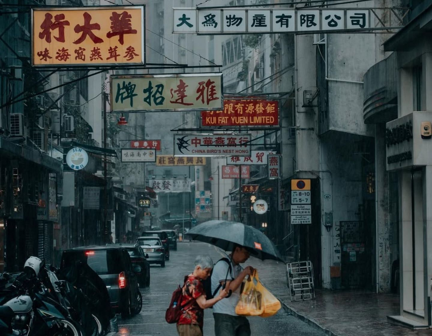 Pedestrians sharing an umbrella on a rain-soaked Hong Kong street