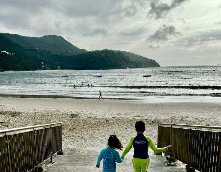 siblings hold hands walking to Clearwater Bay Second Beach in Hong Kong