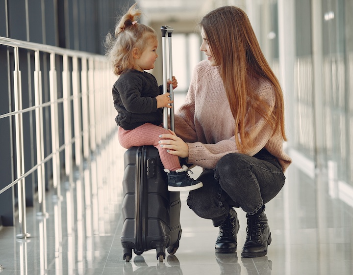mother with baby riding on a carry on suitcase before a flight