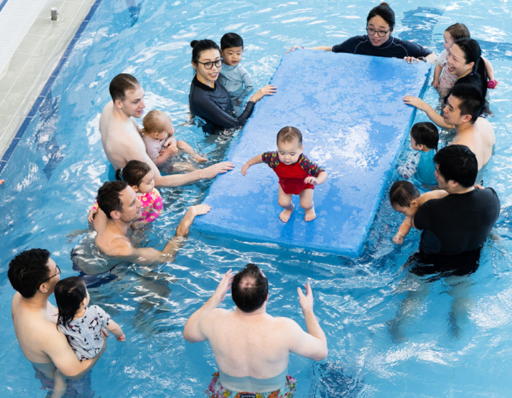 group of adults and toddlers in a pool during a swimming lesson at harry wright swim school hong kong