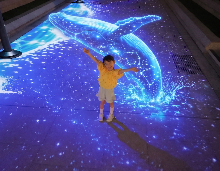 a child poses with a light up humpback whale at mega sky