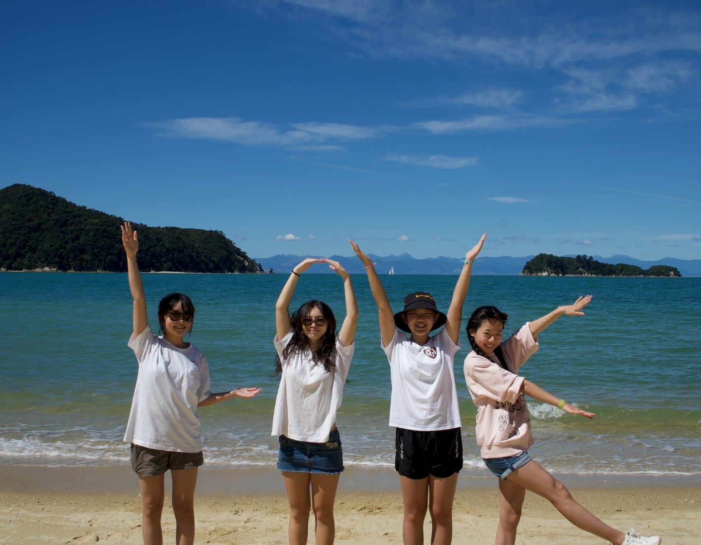 four girls on a beach in Hong Kong spell out LOVE with their arms