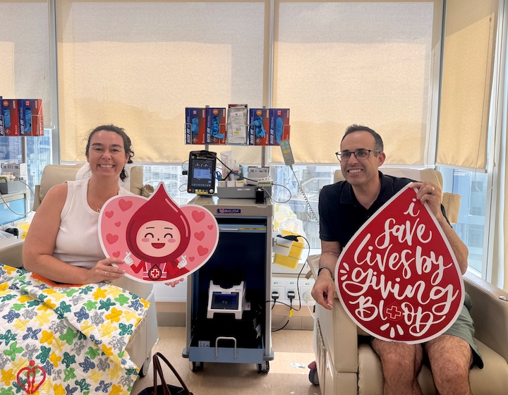 a man and a woman sit in a blood donation chair holding signs after registering to donate bone marrow in Hong Kong