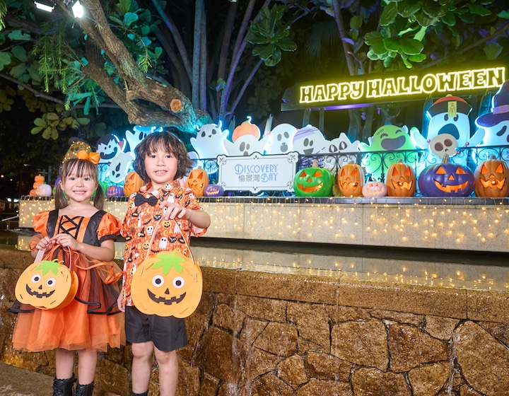 two children in halloween costumes pose in front of halloween decorations in discovery bay