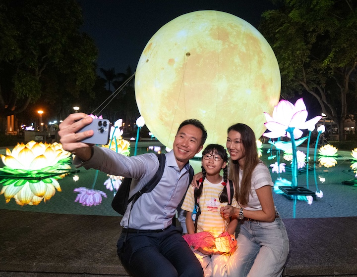a family poses in front of a giant golden moon lantern at Victoria Park Hong Kong during the international lantern festival at Mid Autumn