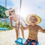 a mother pushes her son on a swing by the beach in Phuket