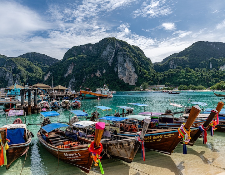 colourful boats on a Phuket beach with turquoise water and lush green mountains behind