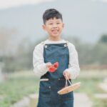 A Chinese boy smiling in a field with a basket of freshly picked strawberries from a Hong Kong strawberry farm