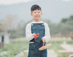 A Chinese boy smiling in a field with a basket of freshly picked strawberries from a Hong Kong strawberry farm