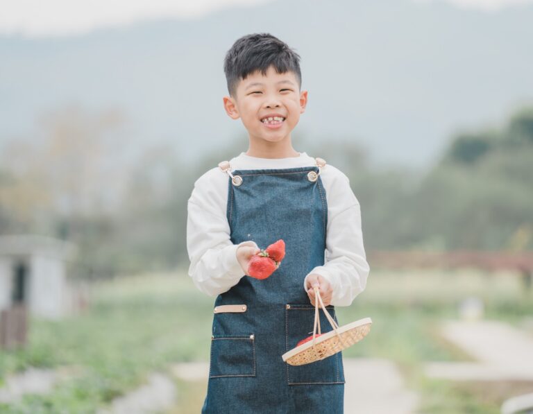 A Chinese boy smiling in a field with a basket of freshly picked strawberries from a Hong Kong strawberry farm