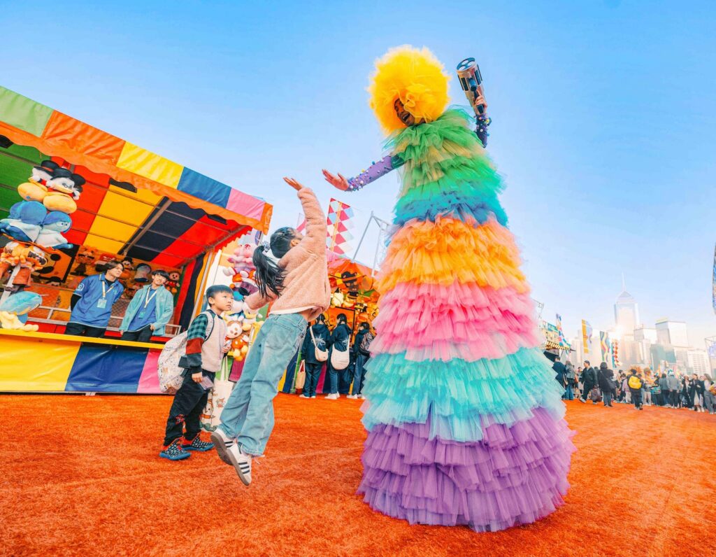 a little girl jumps to high five a performer in a rainbow costume at the Hong Kong aia carnival