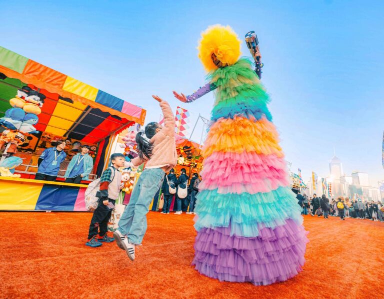 a little girl jumps to high five a performer in a rainbow costume at the Hong Kong aia carnival
