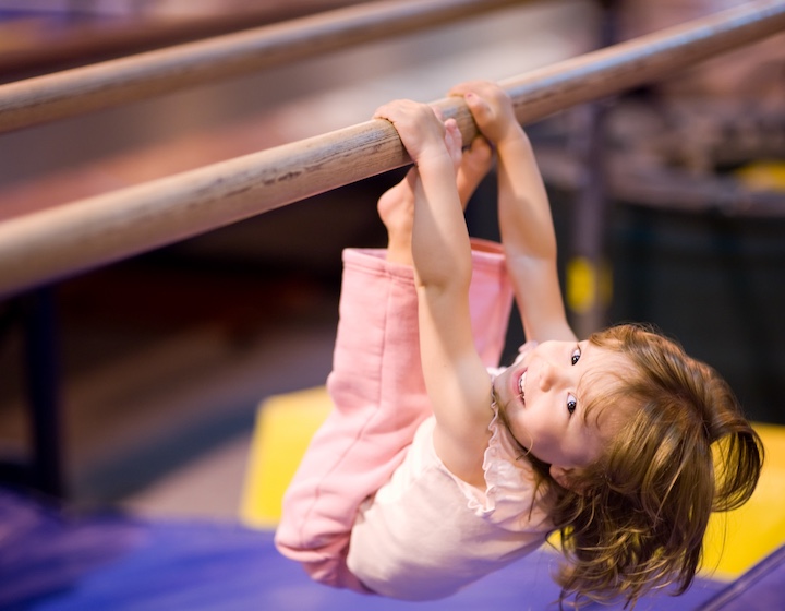a young girl hangs upside down on a bar at a baby gym class in Hong Kong