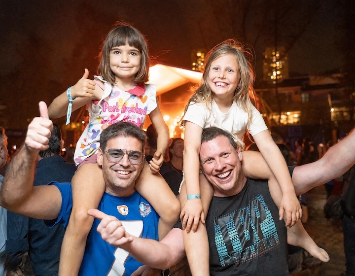 two dads with their girls on their shoulders enjoying the live music at The Big Picnic event in Discovery Bay
