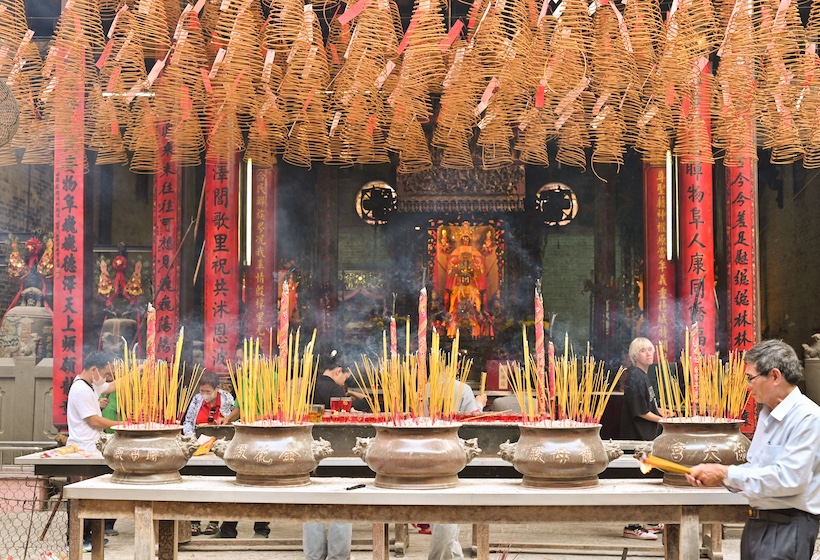 worshippers at a Hong Kong temple full of large incense coils and offerings at the alter