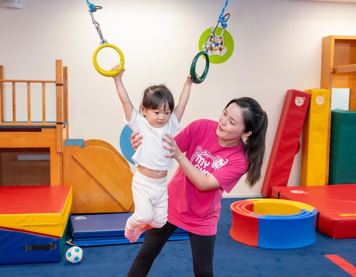 a toddler hangs on the rings with a coach at my gym Hong Kong baby gym class