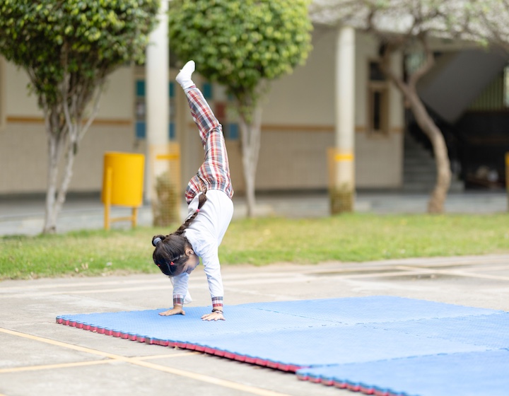 a young girl with a disability does a handstand in a school yard