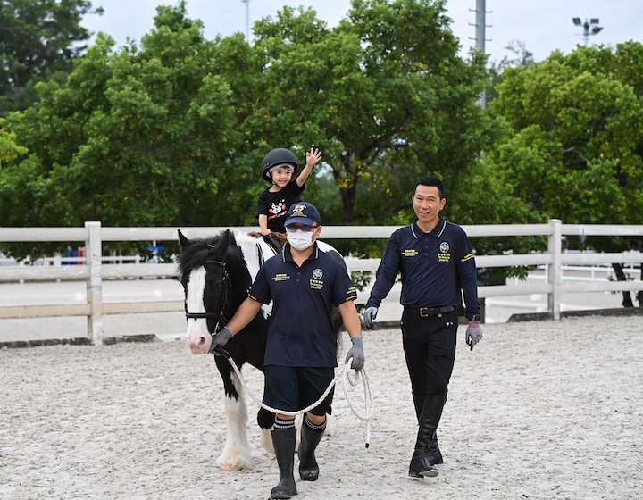 a little boy rides a pony led by two stable hands at the Tuen Mun public horse riding school in Hong Kong